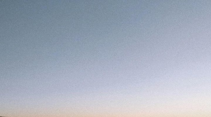 Capture the tranquillity of dusk over an expansive ocean with distant hills silhouetted against a twilight sky.